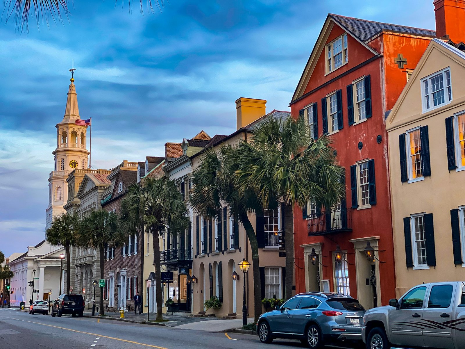 A street view of historic buildings in Charleston, South Carolina, with St. Michael's Church steeple in the background.